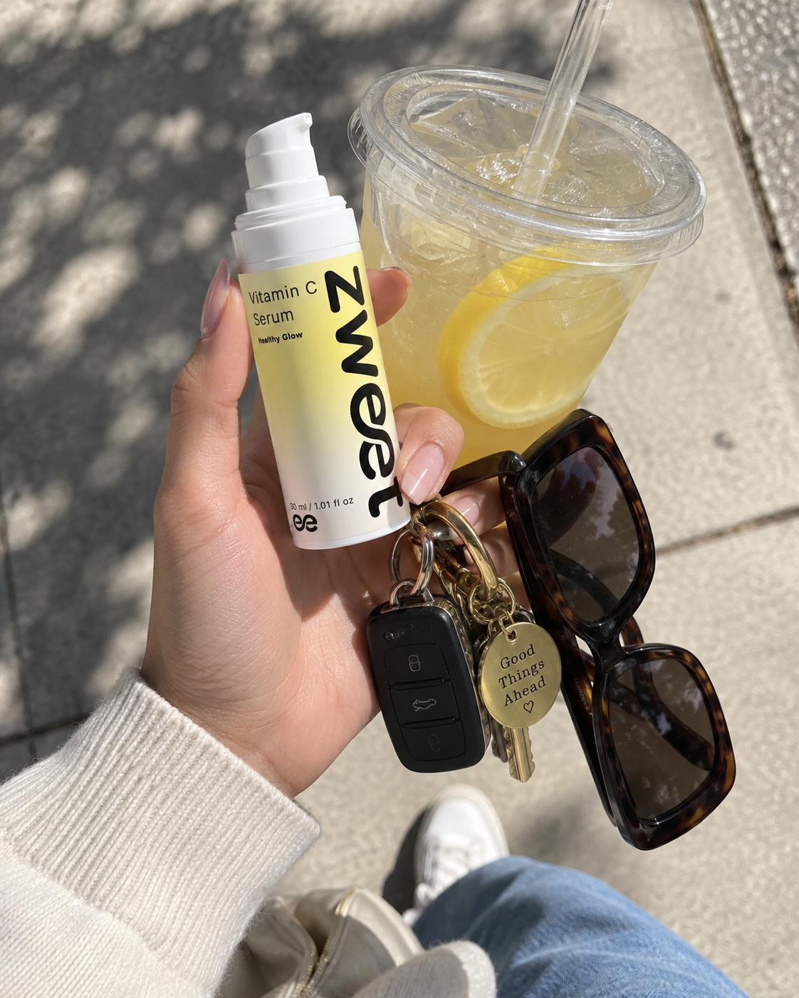 Producto Zweet Cosmetics de vitamina C en mano junto a bebida cítrica para imagen lifestyle de verano
